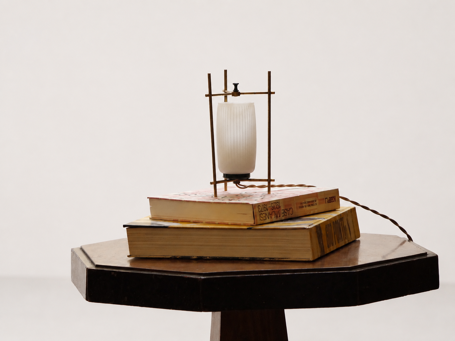 Lampada da tavolo modernista italiana anni ’50 in ottone con diffusore in vetro opalino, ambientata su tavolino con libri.